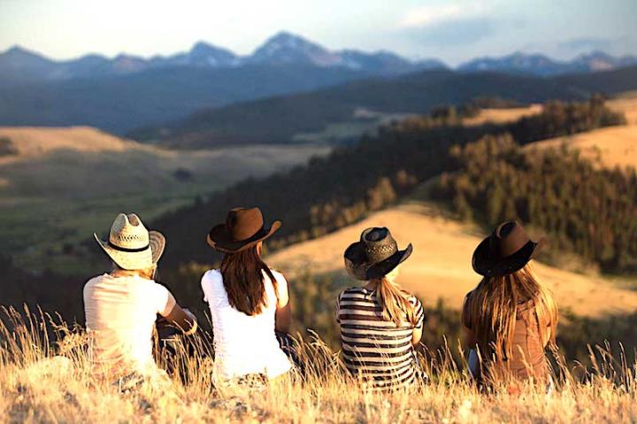 Four people wearing brimmed hats with their backs to the camera looking at a view