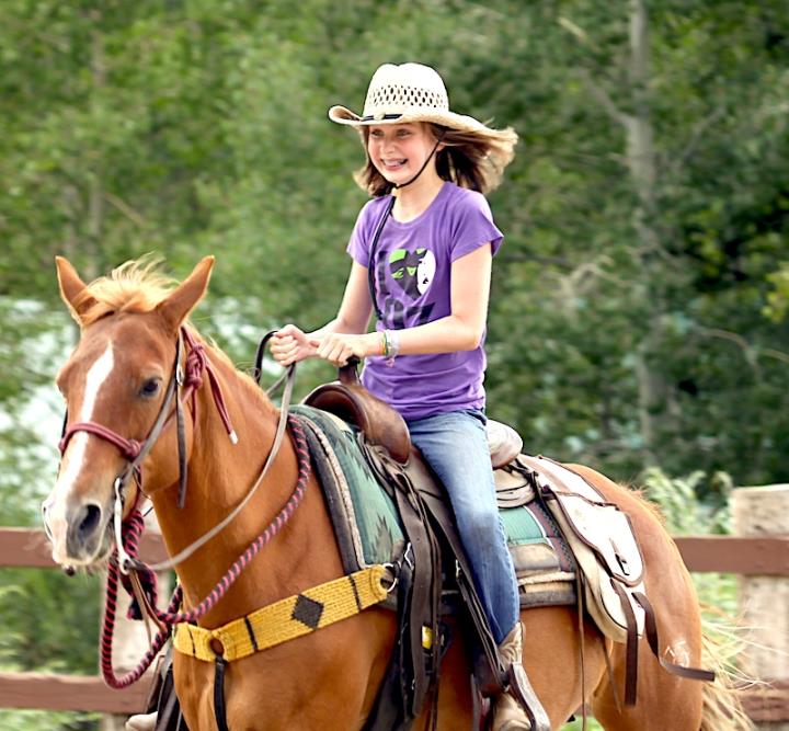 Girl in white hat smiling on horse
